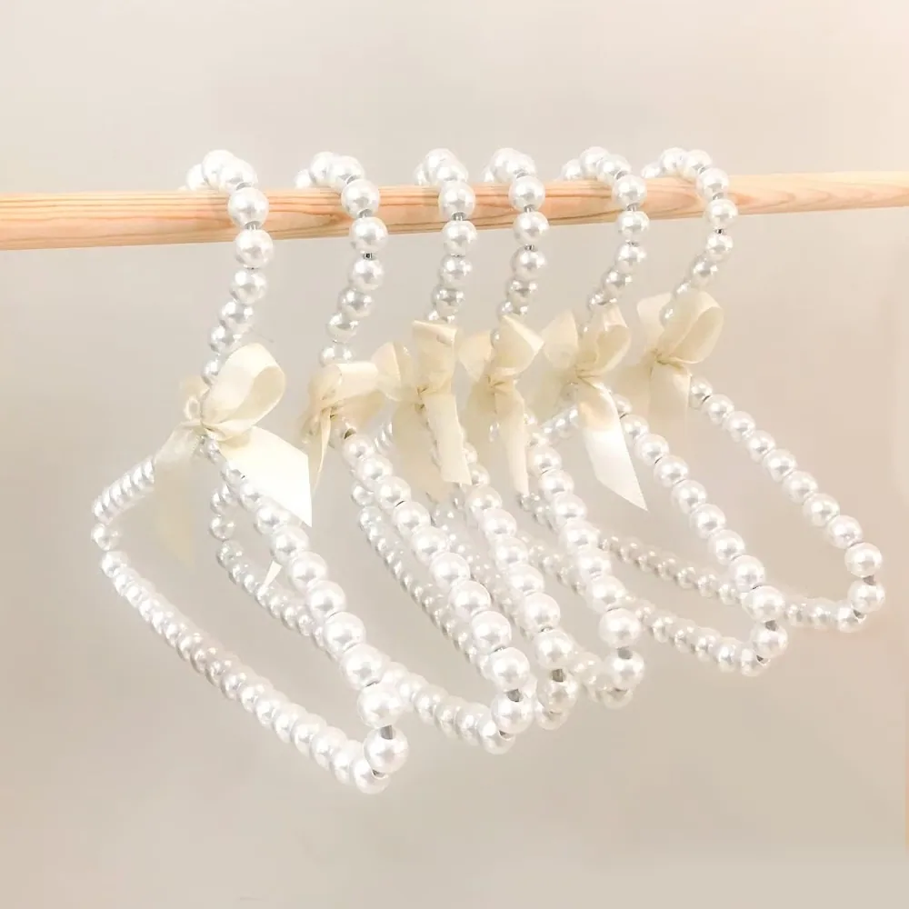 Kids pearl beaded hangers with ivory satin bows holding children's clothes on a wooden rail